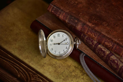 High angle view of pocket watch by book on table
