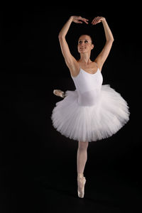 Full length of young woman dancing against black background