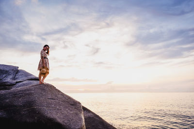 Low angel view of woman standing on rock against sky