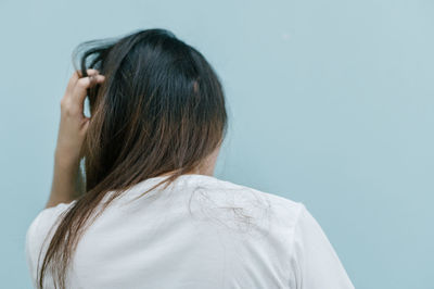 Rear view of woman scratching head against colored background