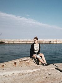 Portrait of woman sitting by harbor against sky