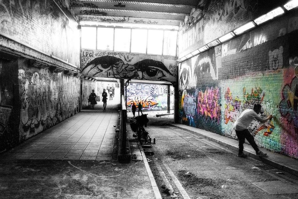 PEOPLE WALKING IN TUNNEL WITH GRAFFITI ON WALL