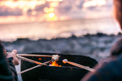 Cropped image of people holding sticks with marshmallow on fire at beach