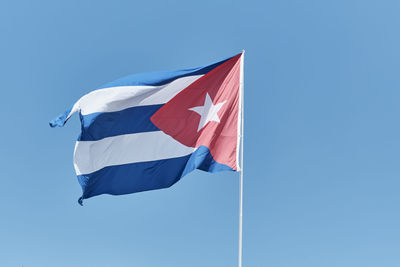 National flag of cuba waving in wind on flagpole over background of blue sky.