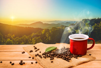 Coffee cup on table by mountains against sky