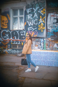 Full length of young woman standing against graffiti wall