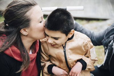 Mother kissing disabled son sitting on wheelchair in yard