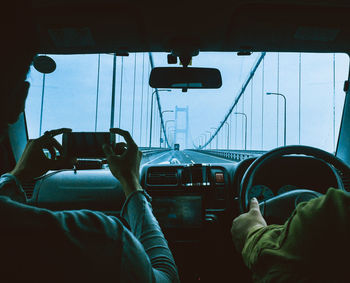 Rear view of man photographing bridge through mobile phone while sitting in car