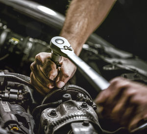 Cropped hands of mechanic repairing engine of car