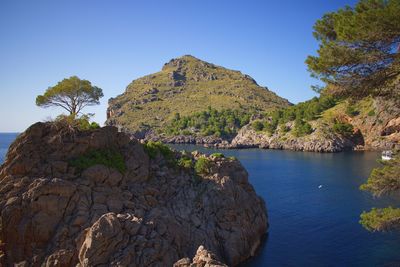 Scenic view of rocks by sea against clear sky