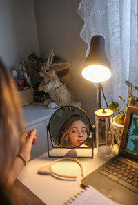Young girl sitting at her desk and looking in her mirror
