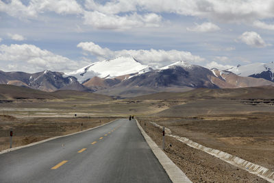 A flat and uninhabited asphalt road leads to the distant snowy mountains