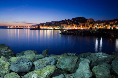 Scenic view of sea by illuminated city buildings against sky