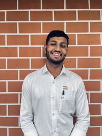 Portrait of smiling young man standing against brick wall