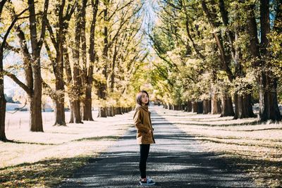 Side view portrait of woman standing on road amidst trees