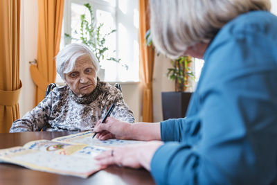 Woman taking care of old woman doing crossword puzzle