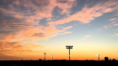 Silhouette floodlight against sky during sunset