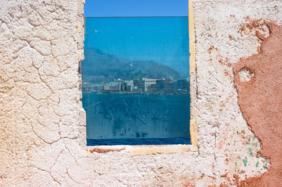 Sea by buildings against mountains seen though glass window