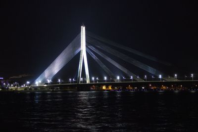 Illuminated bridge over river against sky at night