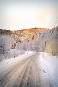 Road by snow covered landscape against sky