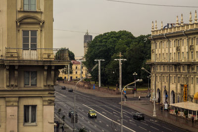 Cars on road by buildings in city against sky