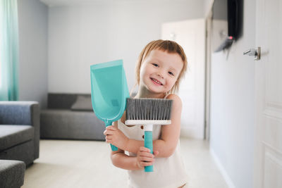 Cute european child with blue scoop for garbage and brush for sweeping floor helps to clean,