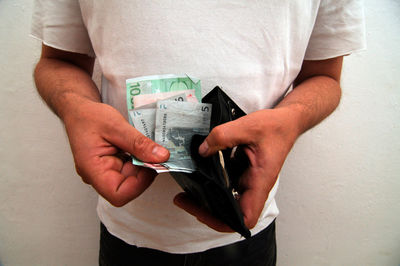 Midsection of man holding paper while standing against wall