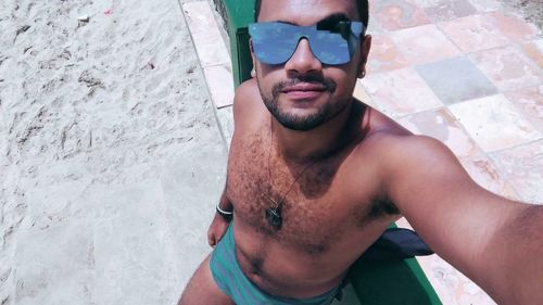 High angle view of shirtless young man standing at beach on sunny day