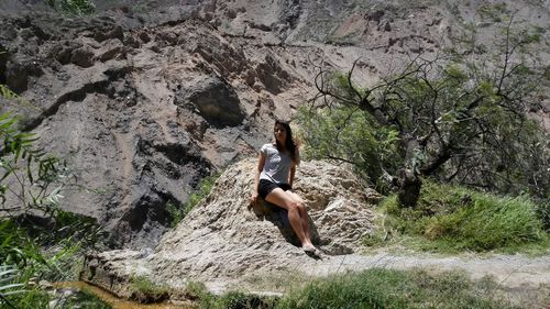 Woman looking away while sitting against rock formation