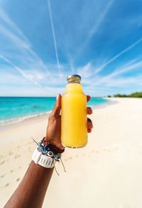 Midsection of person holding sunglasses on beach against sky