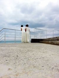 Rear view of women standing by railing against sky