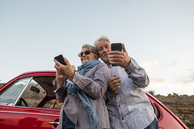 Senior couple taking selfie using smart phone against sky