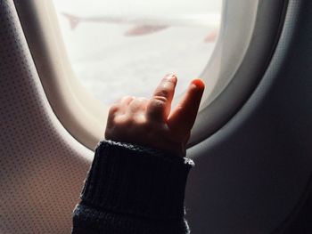 Cropped hand of child gesturing peace sign by airplane window