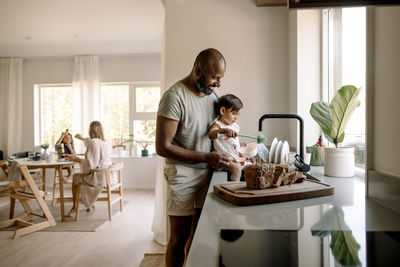 Smiling man standing near daughter washing dishes in kitchen at home