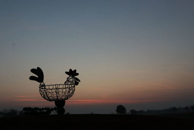 Silhouette of horse sculpture on field against sky during sunset