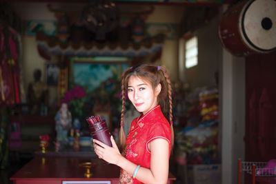 Portrait of young woman holding bottle while standing at home