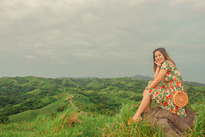 Woman sitting on field against sky