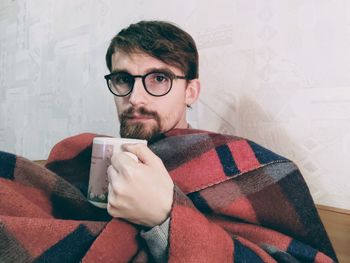 Portrait of young man holding eyeglasses at home