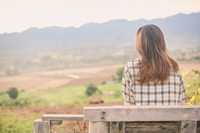 Rear iew point of young woman sitting on chair and looking to faraway with countryside environment