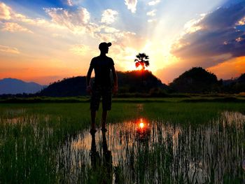 Man standing at farm against sky during sunset