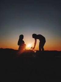 Silhouette friends standing on land against sky during sunset
