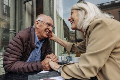 Loving senior woman sitting with man holding hands at sidewalk cafe