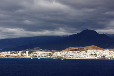 Sea and community by mountains against cloudy sky