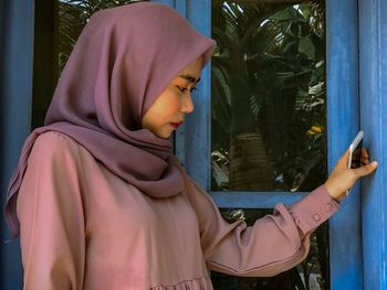 Side view of woman looking down while standing by window