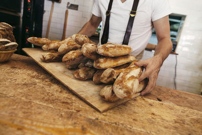 Baker holding tray of fresh baguettes in bakery