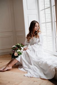 Young woman sitting with flowers on window at home