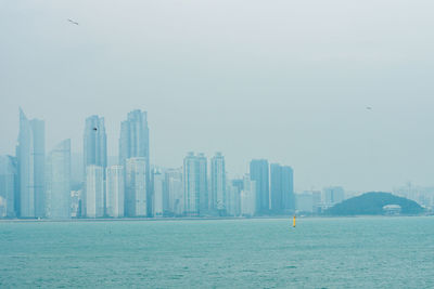 Urban skyline by sea against sky