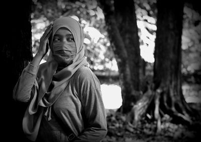 Portrait of young woman standing against tree