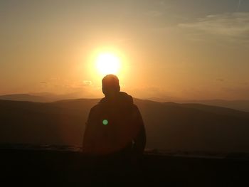 Rear view of silhouette man looking at mountain against sky during sunset