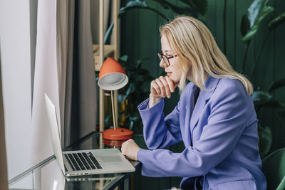 Businesswoman with hand on chin looking at laptop in home office